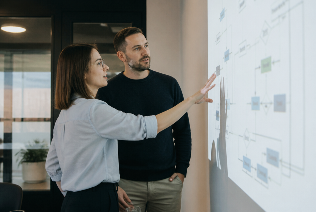 Deux consultants devant un tableau de flux de gestion projeté, en salle de réunion